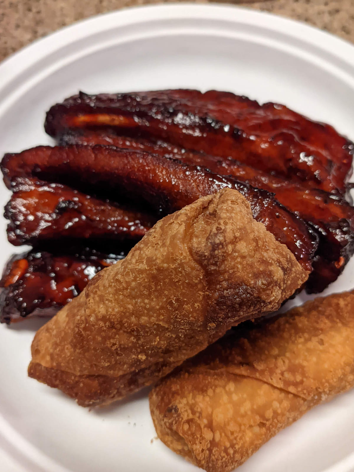 Two blistered egg rolls and glazed barbecue ribs on a white disposable plate, photographed at Peking House in Navarre, Florida.